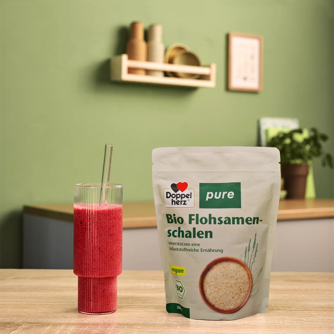 Doppelherz pure Bio Flohsamenschalen neben rotem Smoothie auf Tisch